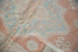 Distressed Oushak rug with geometric motifs in cantaloup, dusty mint, and cream.