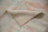 Distressed vintage Oushak rug corner revealing pale mint, cantaloupe geometric patterns and fringe.