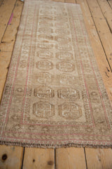 Angled view of distressed vintage Afghani runner, traditional beige elephant guls and pale pink border.