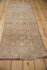 Distressed vintage Afghani Bokhara runner, showcasing its short pile, beige guls, and pale pink striped selvage.