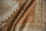 Distressed texture of a vintage Oushak carpet, featuring time-softened sand and cantaloupe geometric motifs.