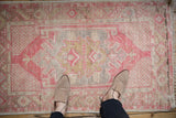 Distressed Oushak rug, faded raspberry and gold geometric medallion, textured pile, with feet for scale.