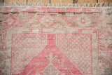 Vintage Oushak rug detail: distressed pink, ivory geometric pattern, mostly even wear, fringe.