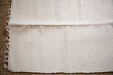 Natural undyed organic cotton rag rug with textured off-white weave and fringe.