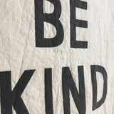 Raised black screenprint 'BE KIND' text detail on natural unbleached cotton banner.