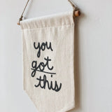 Handcrafted cotton banner detail with natural wood dowel, twine, and raised black 'you' lettering.