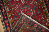 Corner of a vintage Karaja rug folded back to show the hand-knotted weave and rich red geometric pile.