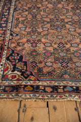 Tattered end of vintage Hamadan rug with dusty blush, navy, and red Herati design.