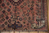 Corner view of vintage Kamseh rug with dusty red field, stylized animal motifs, and striped border.