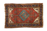 Antique Heriz rug with a stepped blue medallion, serrated leaves, and arrowed finials on a rich brick red field.