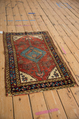 Angled perspective of a small antique Heriz rug with a central stepped medallion in blue on a red field.