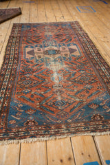 Malayer rug: worn dusty brick red field, aquatic blue spandrel, partial Herati motif.