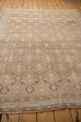 Distressed beige Oushak carpet close-up: muted trellis pattern, floral motifs, and soft abrash texture.