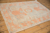 Distressed Oushak rug corner with cantaloupe geometric border and pale blue motifs on ivory.