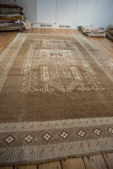 Distressed Kars carpet detail with geometric checkered border and stylized ram's horn motif in brown and ivory.