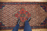 Vintage Hamadan runner, cherry red shield medallion, sand floral lattice field, human feet.