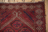 Vintage Beshir rug corner featuring ram's horn guls, deep reds, ivory, and tattered fringe.