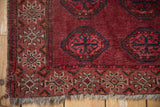 Vintage Turkmen Beshir rug corner, showcasing black cherry red guls and tattered fringe.