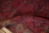 Textured field of ram's horn guls and checkered motifs in cochineal red and navy.