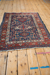 Angled view of a vintage Persian Karaja rug with geometric red and navy blue medallions.