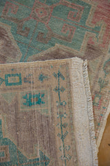 Distressed vintage Oushak runner with even wear on green-blue geometric pile and ivory fringe.