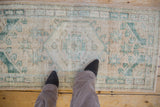 Distressed texture and worn geometric medallion on a cream and faded emerald Oushak runner.