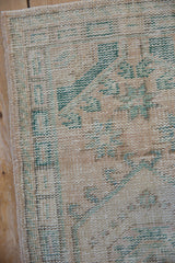 Distressed vintage Oushak runner texture, showing cream and emerald geometric motifs, wear, and side selvage.