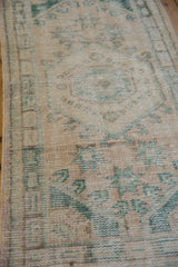 Distressed vintage Oushak rug showing worn geometric motifs in cream and dusty emerald green.
