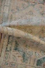 Distressed Oushak rug pile showing cream, dusty emerald patterns, mostly even wear and foundation.