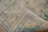 Folded corner of distressed Oushak rug, showing worn pile, colorful foundation, and intact selvage.