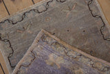 Distressed Oushak rug showing its muted purple foundation, side selvage, and low pile.