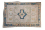 Vintage distressed Oushak rug featuring a blue medallion, beige field, and wave motif borders.