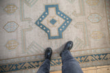 Distressed vintage Oushak rug in beige, dusty blue, and gold, with wave motif border.