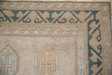 Distressed Oushak rug corner, showing dusty dark denim blue wave border and a partial gold shield-like medallion.