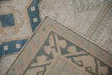 Distressed Oushak rug's beige pile, dusty blue wave border, and side selvage.