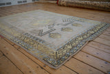 Distressed Melas rug border with geometric primitive patterns, beige, gold, and dusty blue abrashes.