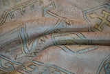 Distressed Melas rug pile featuring geometric primitive motifs in beige, mauve, and blue.