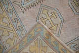 Distressed Melas rug corner, hand-knotted geometric hook and latch patterns in beige and gold.
