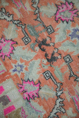 Close-up on the worn, knotted texture of a distressed rug with pops of hot pink and orange.