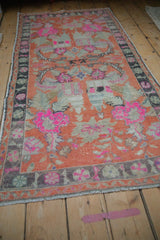 Angled view of a distressed Oushak rug with tangerine, hot pink, and silver floral motifs.