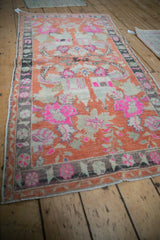 High angle view of a distressed vintage Oushak rug's tangerine and hot pink floral pattern.