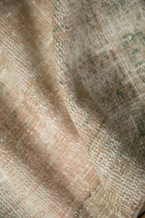 Distressed texture of a vintage Oushak rug with muted cream, brown, and green tones.