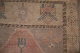 Detail of geometric motifs and distressed pile in dusty rose, dusty teal, and beige.