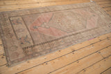 Distressed Oushak runner with dusty rose field, geometric finned plant motif, and faint foundation.
