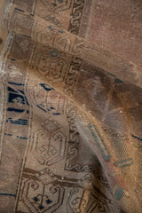 Worn texture of a distressed Oushak rug, with muted rose, beige, and cobalt blue geometric elements.