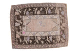 Vintage distressed Oushak rug with a charcoal brown floral border, faded pink field, and stepped corner spandrels.