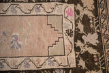 Corner detail of a distressed Oushak rug showing a stepped spandrel and charcoal vine border.