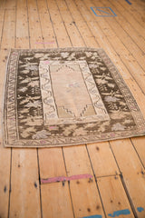 High-angle view of a distressed Oushak rug showing the charcoal brown border and pale ivory field.
