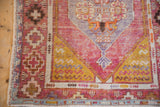 Distressed Oushak rug corner with vibrant faded pink, saffron yellow, and geometric motifs.