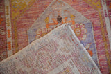 Distressed Oushak rug, showing faded purple, yellow, orange pile and hand-knotted foundation.